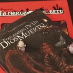 Fotografía del libro Pobladores de un Dios Muerto sobre la mesa, acompañado de dados y el manual de La Marca del Este al fondo.
