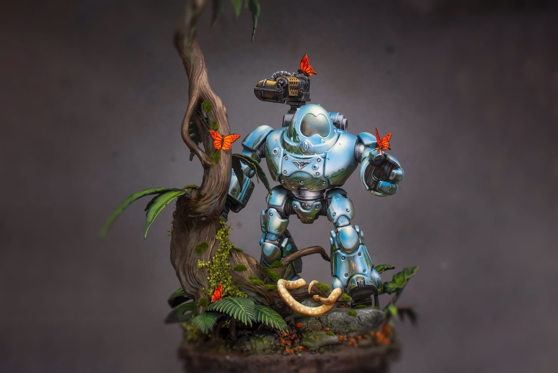 Miniatura pintada con técnica NMM por Juan Sanz, El Miniaturista, representando un robot azul en un entorno natural con vegetación y mariposas.