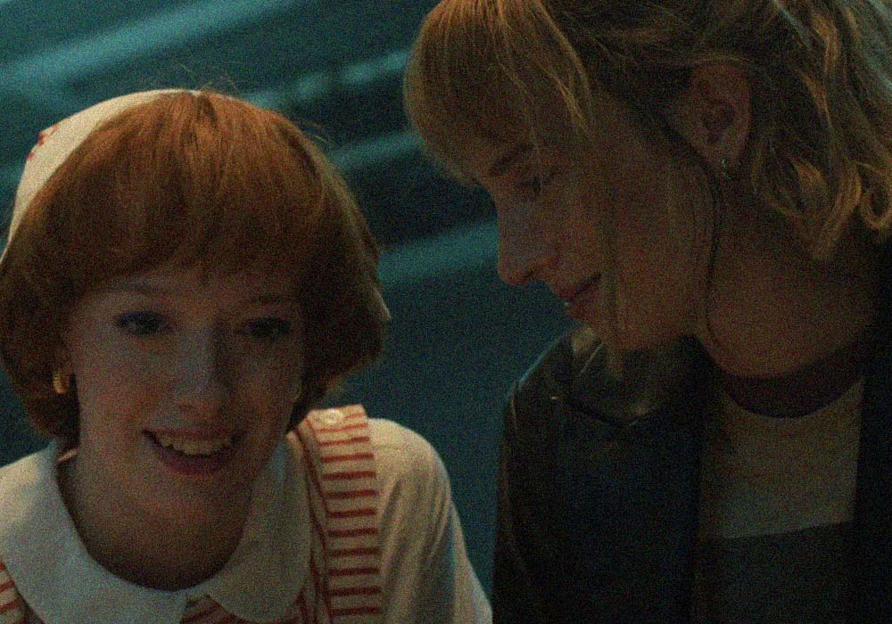 Dos jóvenes en interior con estética ochentera e iluminación fría, compartiendo un momento cercano y cómplice.