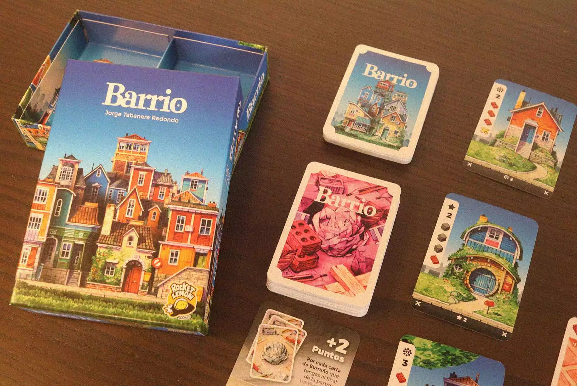 Caja y cartas del juego de mesa Barrio dispuestas sobre una mesa mostrando materiales y casas