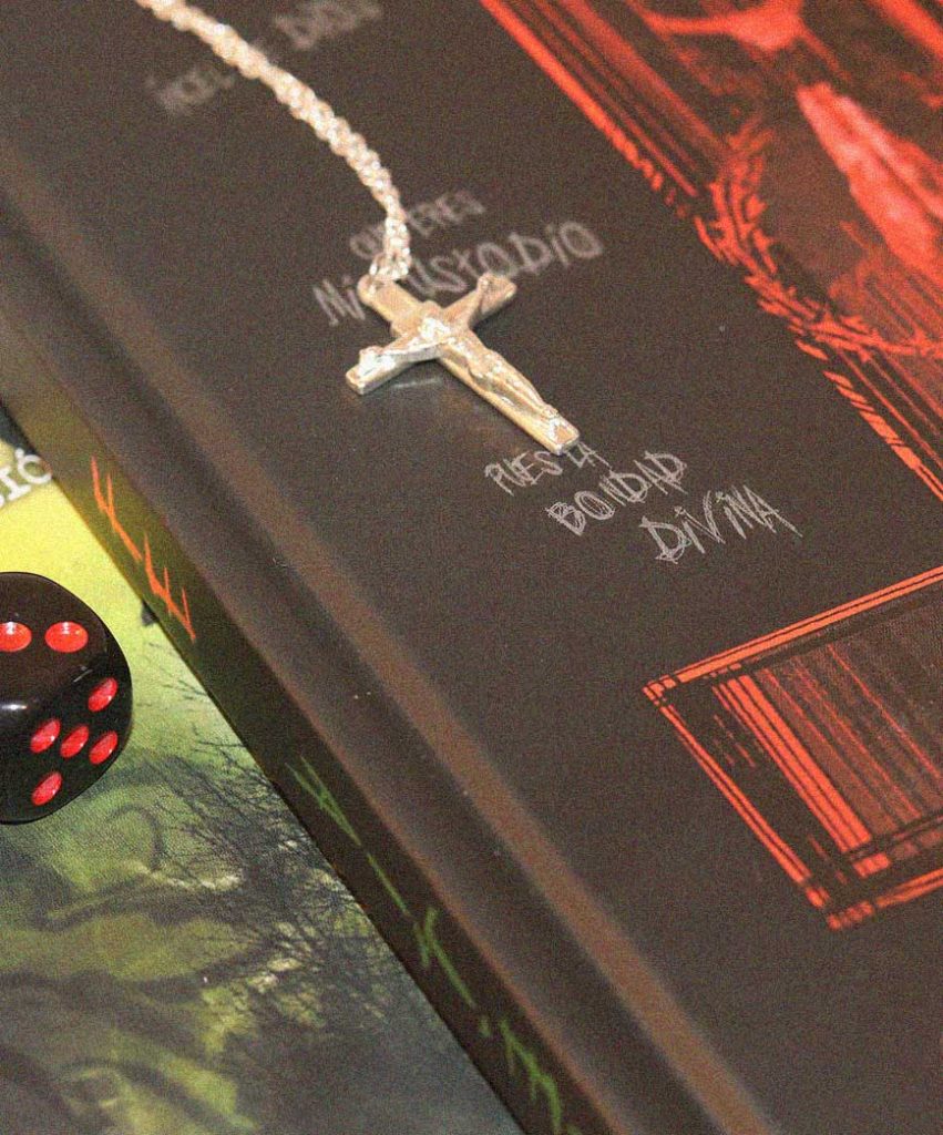 Crucifijo sobre la portada de Fe junto a un dado negro durante una partida de rol.