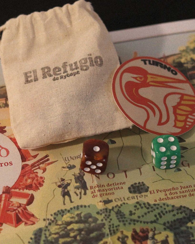 Libro de Alegres Forajidos junto a dados de seis caras y material promocional sobre una mesa de juego.