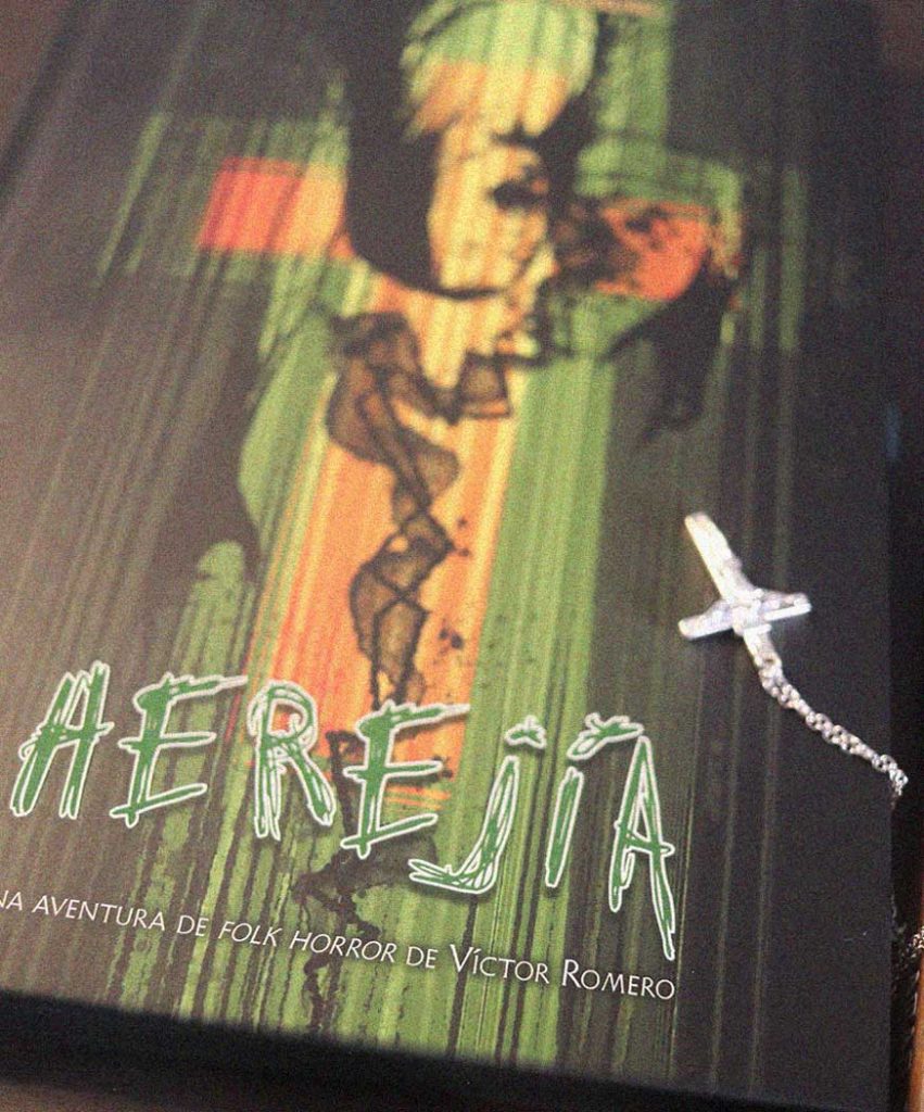 Portada de Herejía, aventura de folk horror escrita por Víctor Romero, junto a un rosario y una cruz sobre una mesa.