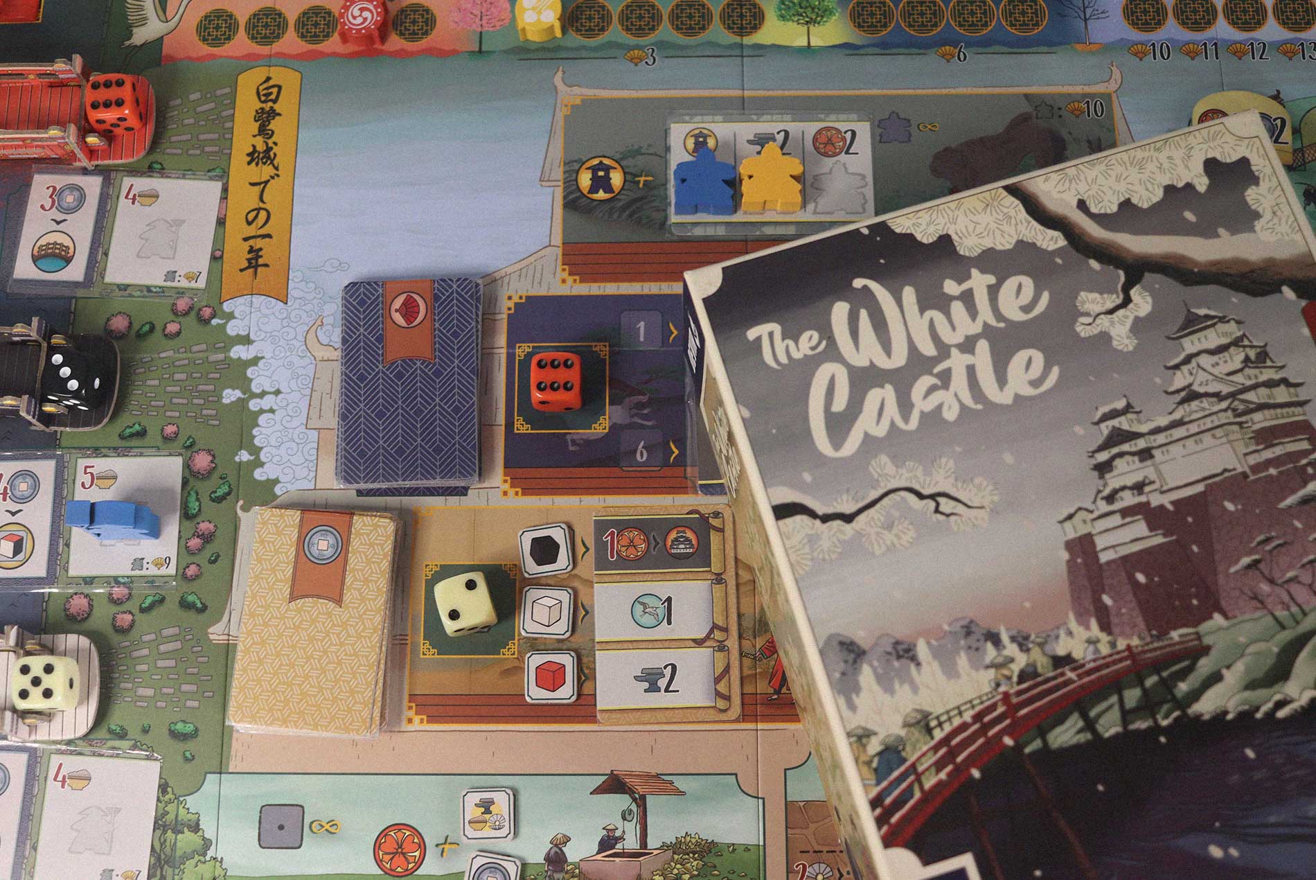 Partida de The White Castle desplegada sobre la mesa, con dados, cartas y la caja del juego sobre el tablero ambientado en el castillo de Himeji.
