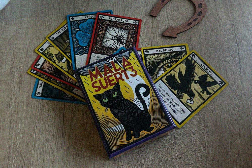 Mala Suerte, juego de mesa de Nico Cardona ilustrado por Tomás Hijo, junto a varias cartas de supersticiones